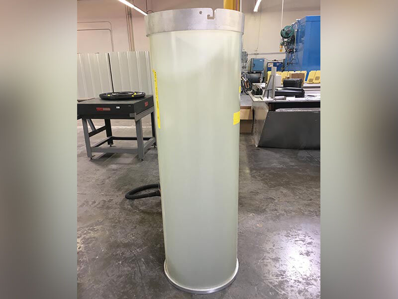 Image shows a 5G lamp post radome standing upright in a manufacturing bay. The radome is a very tall, translucent white tube that has aluminum rings attached the the top and bottom at the ends.